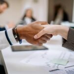 Diverse business professionals exchanging handshake in an office environment, symbolizing agreement.
