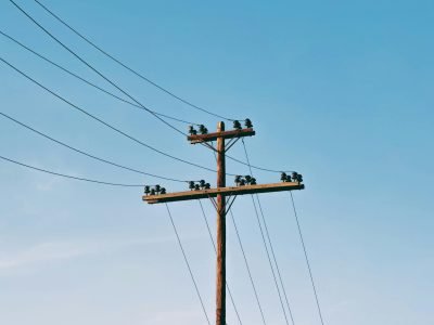 Electrical pole with power lines under a clear blue sky, minimal clouds.