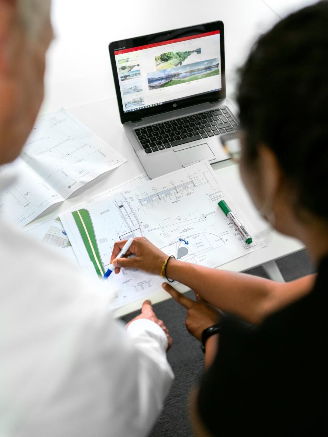 Engineers collaborate on designs with blueprints and laptops in a modern office setting.